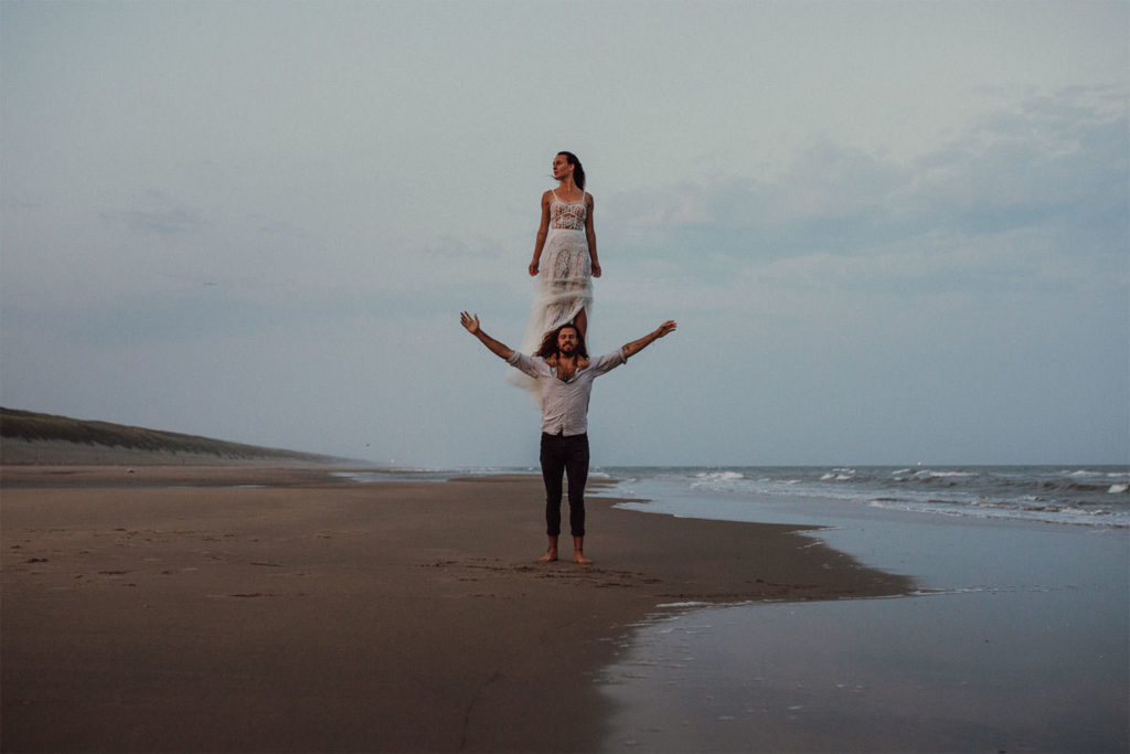 Warum ein After Wedding Shooting eine großartige Ergänzung für eure Hochzeitsfotos ist 5 Brautpaar spaziert Hand in Hand am Strand, umgeben von einer dramatischen Meereskulisse bei Dämmerung.